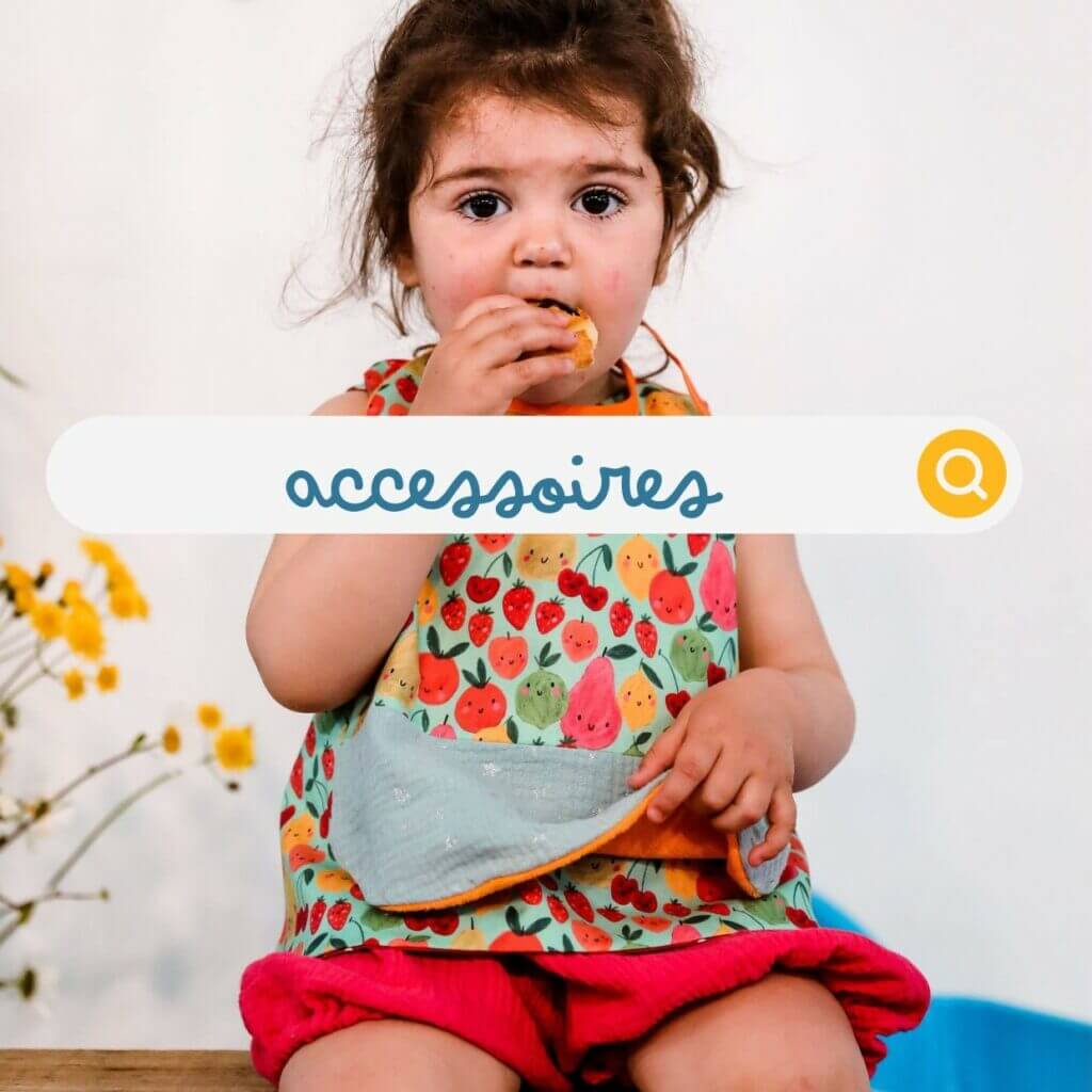 fillette avec un bavoir coloré et imprimé fruits en train de manger pour un repas tout en gardant ses vetements bien propres